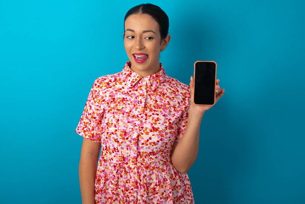Foto von hübschen hübschen Frau trägt florales Kleid über blauem Studiohintergrund demonstrieren Telefon Bildschirm halten Haarschwänze - Foto, Bild