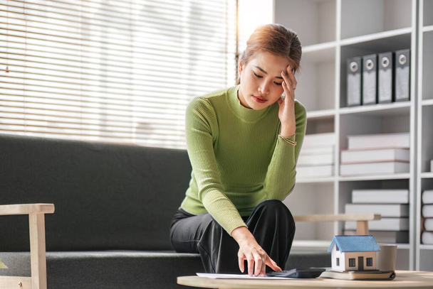 Mujer asiática seria y estresada revisando sus cuentas de gastos mensuales en una sala de estar... - Foto, imagen