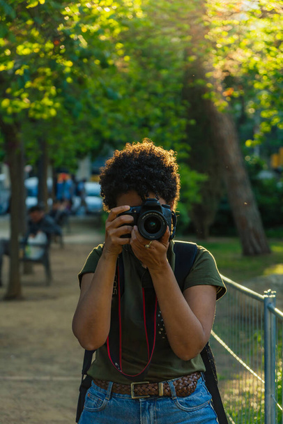 Onnellinen nuori musta Afrikkalainen Amerikkalainen valokuvajournalisti tumma kihara tukka ottaa valokuvan katsomalla kameraa vihreässä puistossa auringonlaskun aikaan auringonlaskun tarkennus rengas takana - Valokuva, kuva