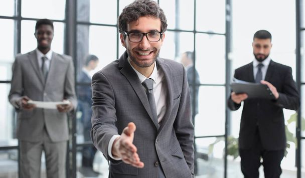 Head shot portrait smiling businessman offering handshake, standing with extended hand in modern office - Fotó, kép