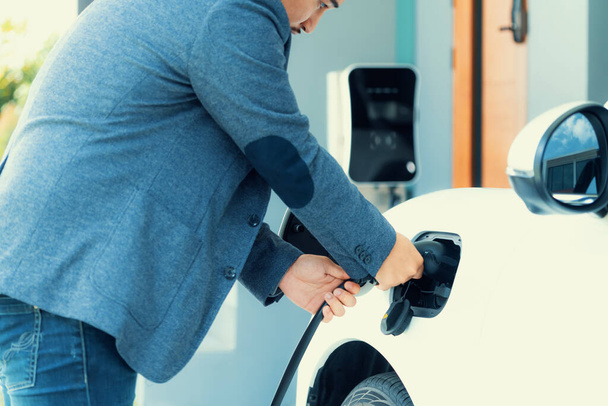 Progressive asian man install cable plug to his electric car with home charging station in the backyard. Concept use of electric vehicles in a progressive lifestyle contributes to clean environment. - Fotoğraf, Görsel
