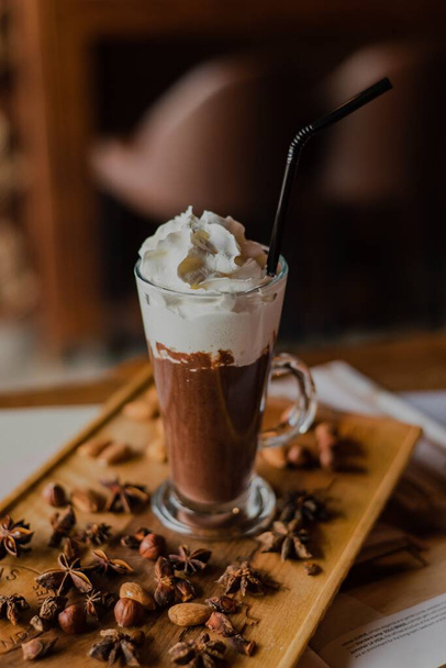 A close-up hot chocolate in a tall glass with whipped cream on a wooden board in a cafe - 写真・画像
