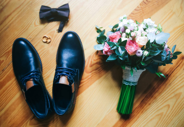 Svatební doplňky. Ženichovy boty s kyticí na dřevěném pozadí. Zlaté prsteny a motýlek jsou poblíž. Stylové věci. - Fotografie, Obrázek