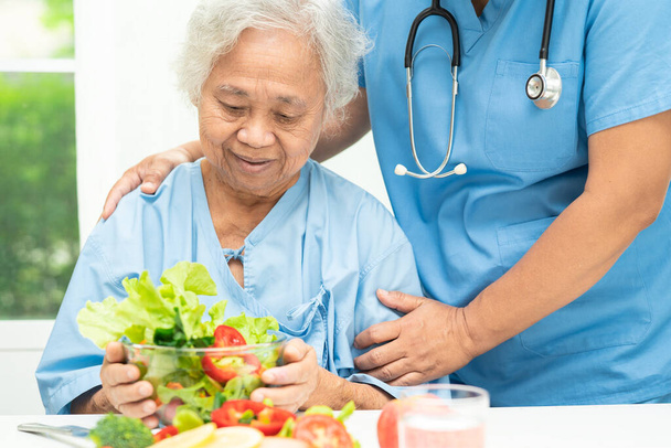 アジアの高齢女性患者病院で野菜の健康食品とサーモンステーキ朝食を食べる. - 写真・画像