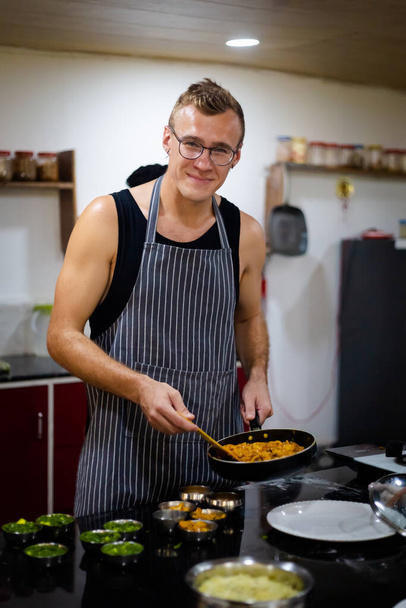 インド料理を提供する若いハンサムな白人男性。ゴアでの料理教室で採取した新鮮な食材を使った伝統的なインド料理の写真 - 写真・画像