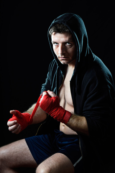 Man in boxing hoodie jumper with hood on head wrapping hands wrists before gym training - Photo, image