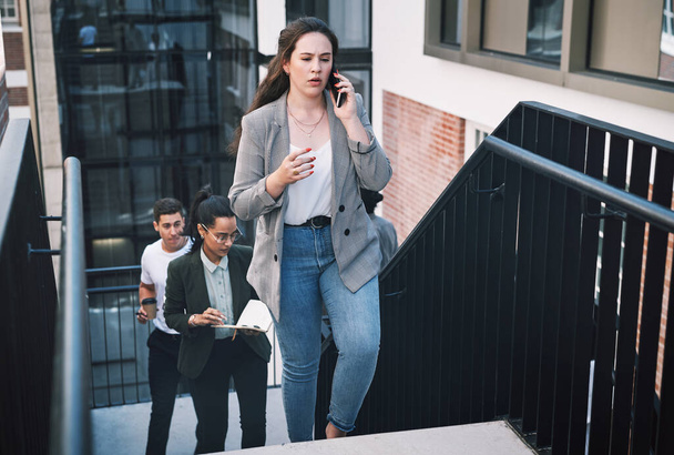 Never let fear hold you back from moving forward. a young businesswoman looking using a smartphone while walking up the stairs in a modern workplace - Valokuva, kuva