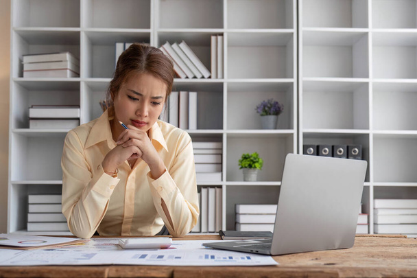 Zestresowana młoda azjatycka bizneswoman skupia się na ponownym sprawdzeniu raportu biznesowego planu inwestycji finansowych przy biurku... - Zdjęcie, obraz