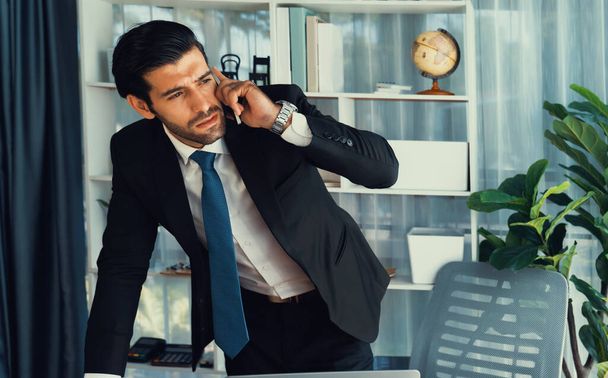 Diligent businessman busy talking on the phone call with clients while working with laptop in his office as concept of modern hardworking office worker lifestyle with mobile phone. Fervent - 写真・画像