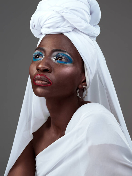 Stilvoll im Kopftuch. Studioaufnahme einer attraktiven jungen Frau, die in traditioneller afrikanischer Kleidung vor grauem Hintergrund posiert - Foto, Bild