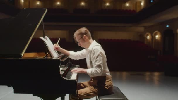 Увеличить фотографию профессионального композитора, пишущего ноты на рояле на сцене пустого концертного зала - Кадры, видео