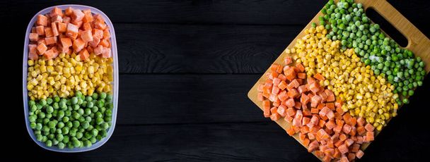 Frozen vegetables in the box and on the cutting board on the black wooden background. Top view. Copy space. - Фото, изображение