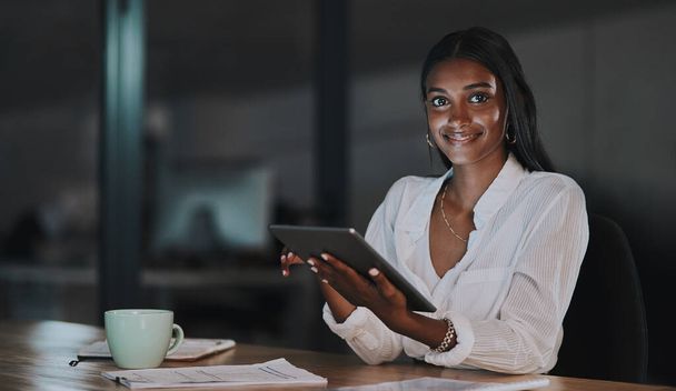 Now you can make smart moves like everyone else. Portrait of a young businesswoman using a digital tablet in an office at night - Fotografie, Obrázek