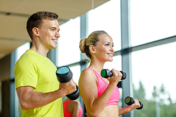 smiling man and woman with dumbbells in gym - Foto, afbeelding