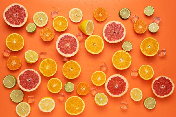 Concept for fresh, fruity and juicy fruit. Top view. Fresh sliced and halved citrus fruits spread with clear ice cubes and water drops on orange background. - Foto, Bild