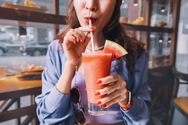 A girl drinks a watermelon smoothie in a cafe through a straw - Valokuva, kuva