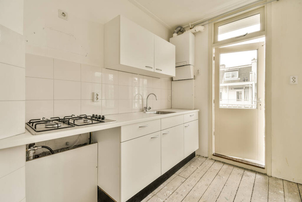 keittiö, jossa on valkoiset kaapit ja laitteet pöydällä tyhjässä huoneessa, jota käytetään ruoanlaittoon - Valokuva, kuva
