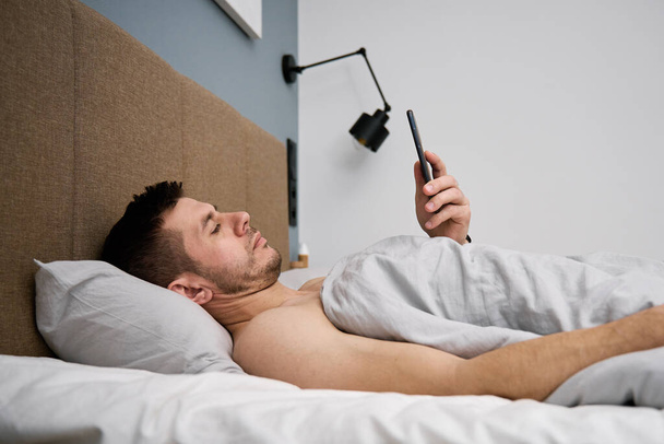 La dépendance au téléphone. Homme couché au lit avec smartphone. Homme se reposant dans la chambre à coucher en utilisant un téléphone portable - Photo, image