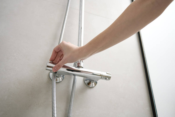 Female hand turn on shower faucet. Modern shower set in bathroom interior. Hygiene concept - Foto, afbeelding