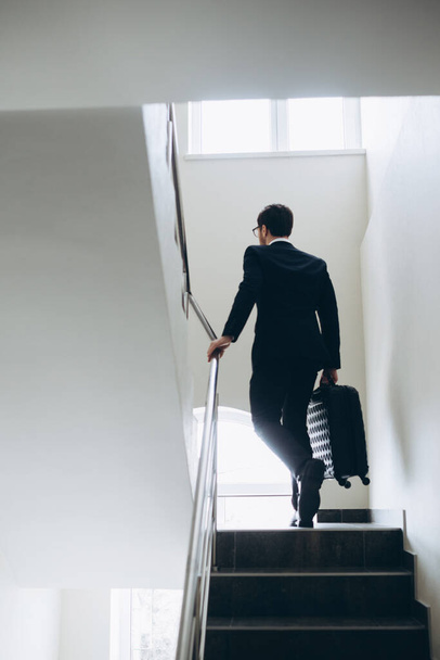 Ένας επιχειρηματίας με βαλίτσα ανεβαίνει τις σκάλες του ξενοδοχείου.. - Φωτογραφία, εικόνα