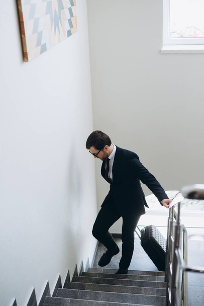 A businessman with a suitcase is walking up the stairs in the hotel. Top view. - Photo, Image