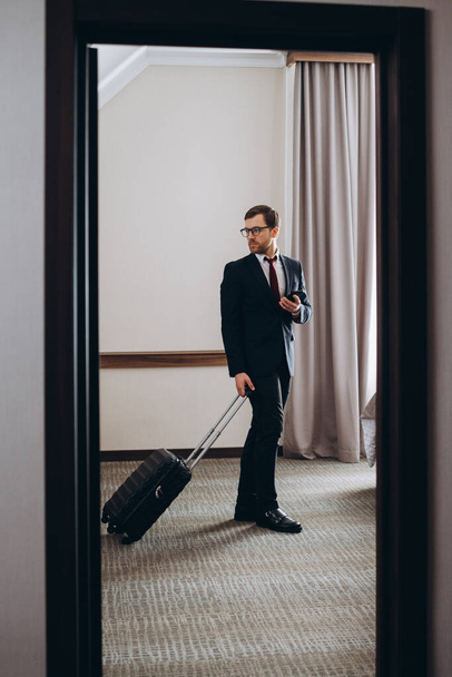 Бизнесмен с чемоданом входит в гостиничный номер. - Фото, изображение