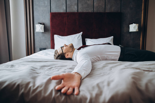 Εξαντλημένος επιχειρηματίας που αναπαύεται στο κρεβάτι μετά από μεγάλη πτήση, τζετ λαγκ. - Φωτογραφία, εικόνα
