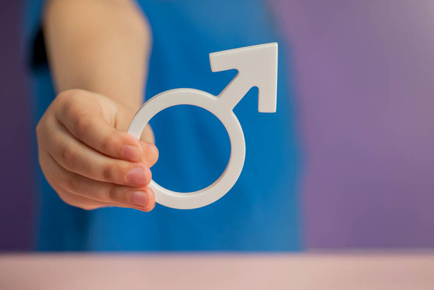 Понятие пола. Мужской половой символ в руке на фиолетовом фоне с копировальным пространством. Высокое качество фото - Фото, изображение