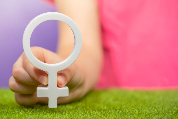 Понятие пола. Женский гендерный символ в руке на фиолетовом фоне в розовой футболке с копировальным пространством. Высокое качество фото - Фото, изображение