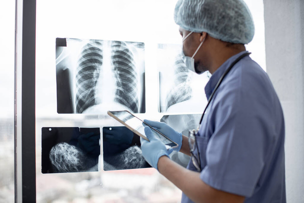 スタイラスペンでタブレットを使用して保護服で多人種医療従事者によって研究胸部X線検査に焦点を当てます。技術を用いて左肺の質量を識別する男性放射線医. - 写真・画像
