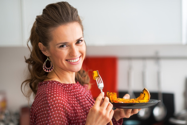 Πορτρέτο της νεαρής γυναίκας που τρώει ψημένο κολοκύθα στην κουζίνα - Φωτογραφία, εικόνα