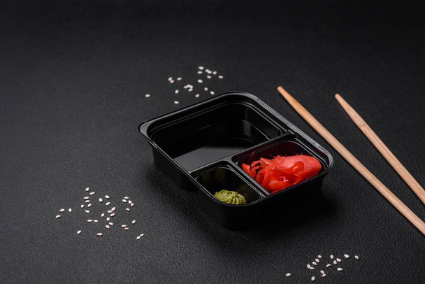 Pickled ginger, soy sauce and wasabi in portioned plastic containers on a dark concrete background - Foto, Imagem