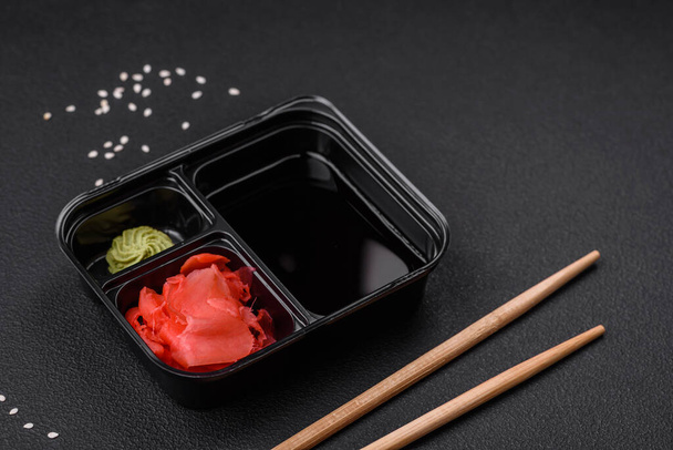 Pickled ginger, soy sauce and wasabi in portioned plastic containers on a dark concrete background - Fotó, kép