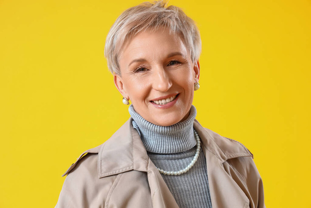 Beautiful mature woman in coat on yellow background, closeup - Foto, Bild