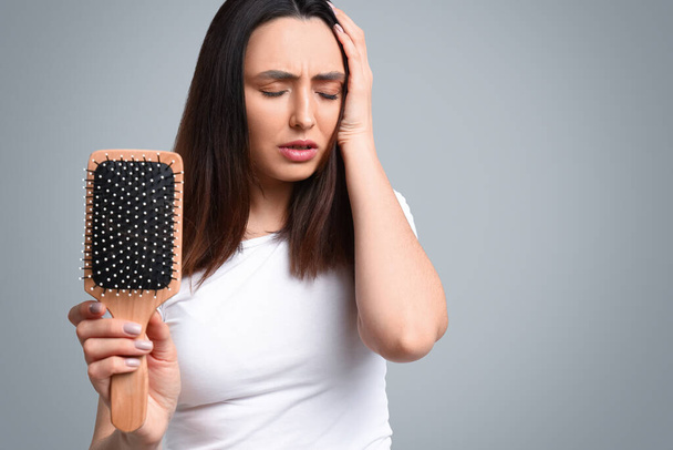 Занепокоєна молода жінка з проблемою випадання волосся на сірому фоні
 - Фото, зображення