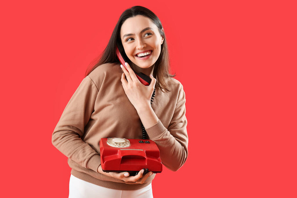 Pretty young woman talking by telephone on red background - Foto, afbeelding