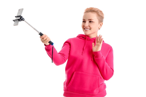 Mujer joven con teléfono móvil tomando selfie sobre fondo blanco - Foto, imagen