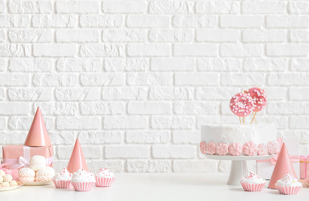 Birthday cake with sweets on white table near brick wall - Photo, Image