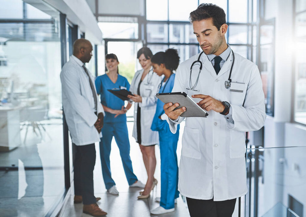 Lekarstwa w erze cyfrowej. młody lekarz korzystający z tabletu cyfrowego w szpitalu z kolegami w tle - Zdjęcie, obraz