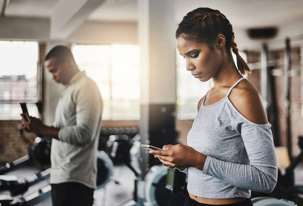 Fitness facilitado con aplicaciones inteligentes. una joven usando un teléfono móvil en un gimnasio - Foto, Imagen