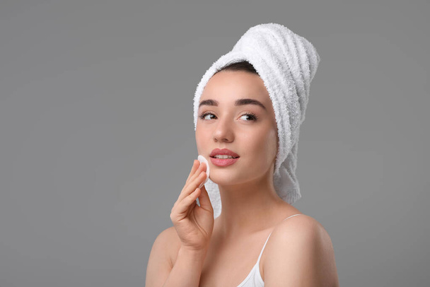 Beautiful woman in terry towel removing makeup with cotton pad on gray background, space for text - Foto, afbeelding