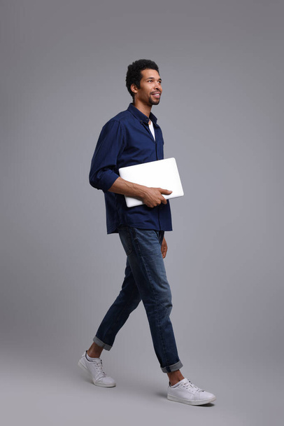 Happy man with laptop walking on grey background - Foto, Bild