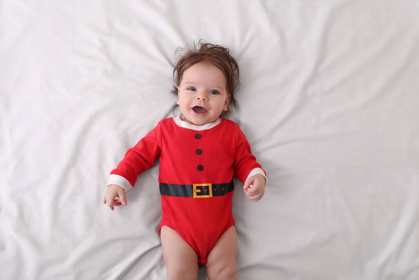 Cute baby wearing festive Christmas costume on white bedsheet, top view - Fotó, kép