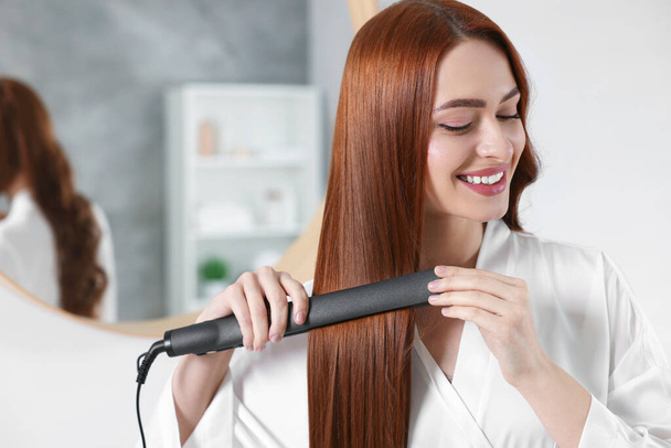 Beautiful woman using hair iron in room, space for text - Фото, зображення