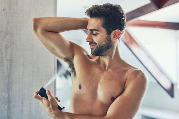 When you smell great you feel great. a cheerful young man without a shirt spraying deodorant under his one armpit in the bathroom - Foto, Imagem