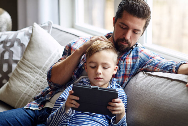 Γνωρίζετε τι κάνουν τα παιδιά σας στο διαδίκτυο; ένα μικρό αγόρι που χρησιμοποιεί ένα ψηφιακό tablet με τον πατέρα του στο σπίτι - Φωτογραφία, εικόνα