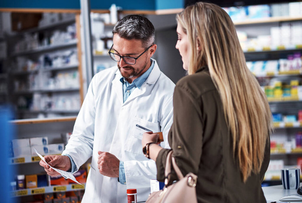 Ceux-ci viennent avec des instructions spécifiques. un pharmacien mature aidant une jeune femme dans un chimiste - Photo, image