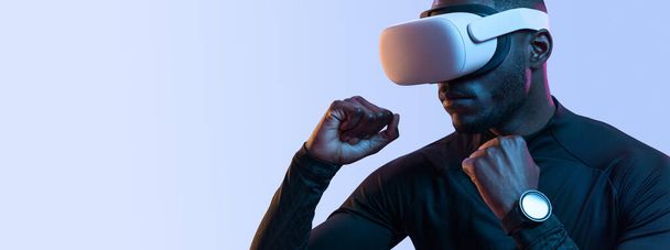 Crop young brutal African American male gamer in stylish clothes and VR glasses boxing against purple background while playing video game - Foto, immagini
