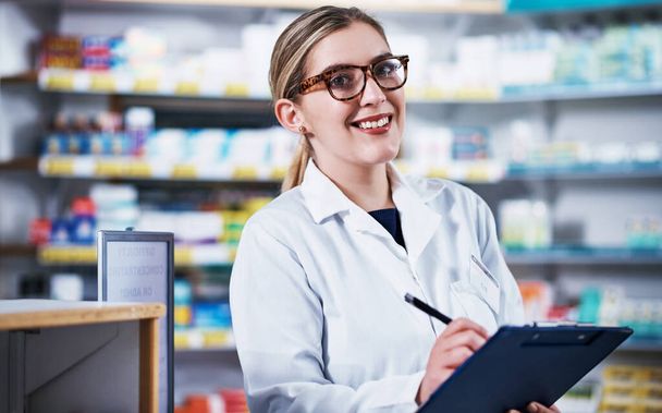Operating a well organized pharmacy. Portrait of a young pharmacist writing on a clipboard in a pharmacy - Photo, Image