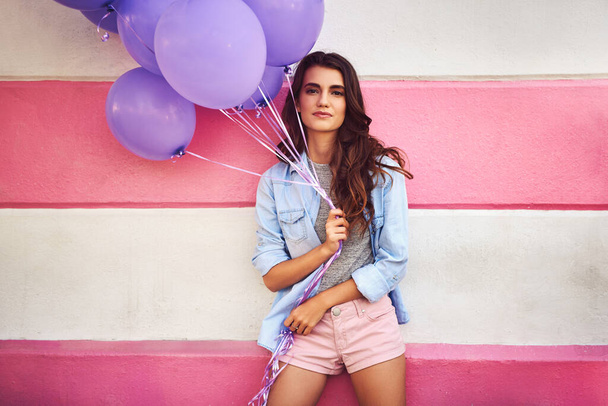Balloons will make anyone happy. a beautiful young woman holding purple balloons against a wall outside - Foto, afbeelding